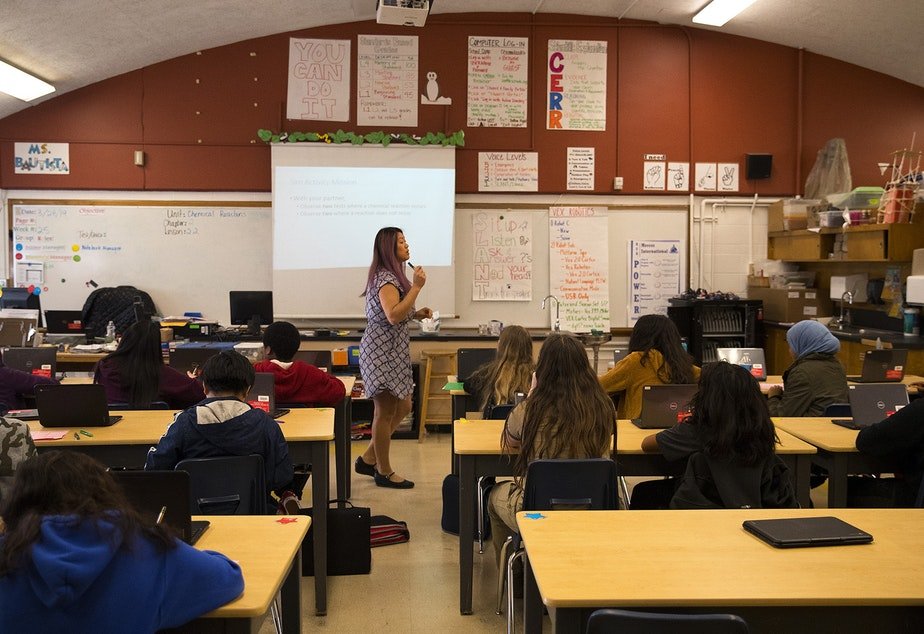 A teacher at the front of the classroom discusses how substances change into different substances during chemical reactions during her 7th-grade science class.