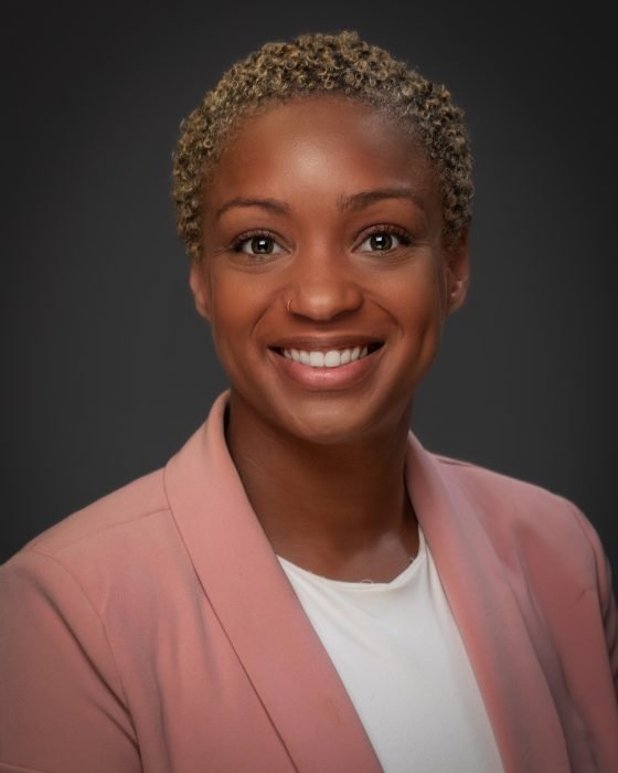 Black woman in her late 30's with short hair, wearing a mauve blazer smiling at the camera