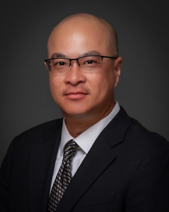 An Asian male in his 40's, bald with glasses, stately looking in black blazer.