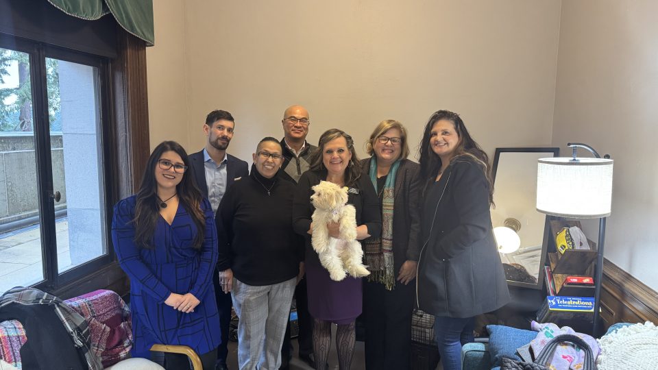 A group of people standing and smiling at the camera. One person is holding a small white dog.