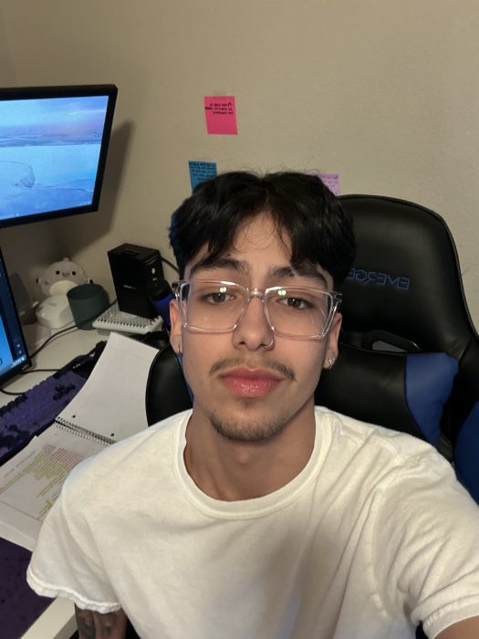Casey Diaz Herrera, a Mexican-American man in his early twenties, he has glasses with medium length hair; wearing a white shirt smiling at the camera