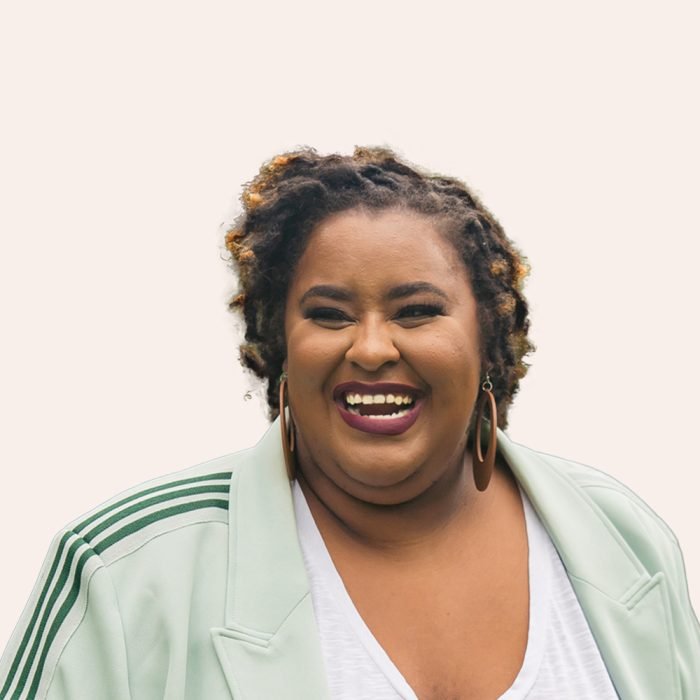 Morgan E Dawson, a black woman in her 30s with small black locs with blonde tips in ateal blazer smiling