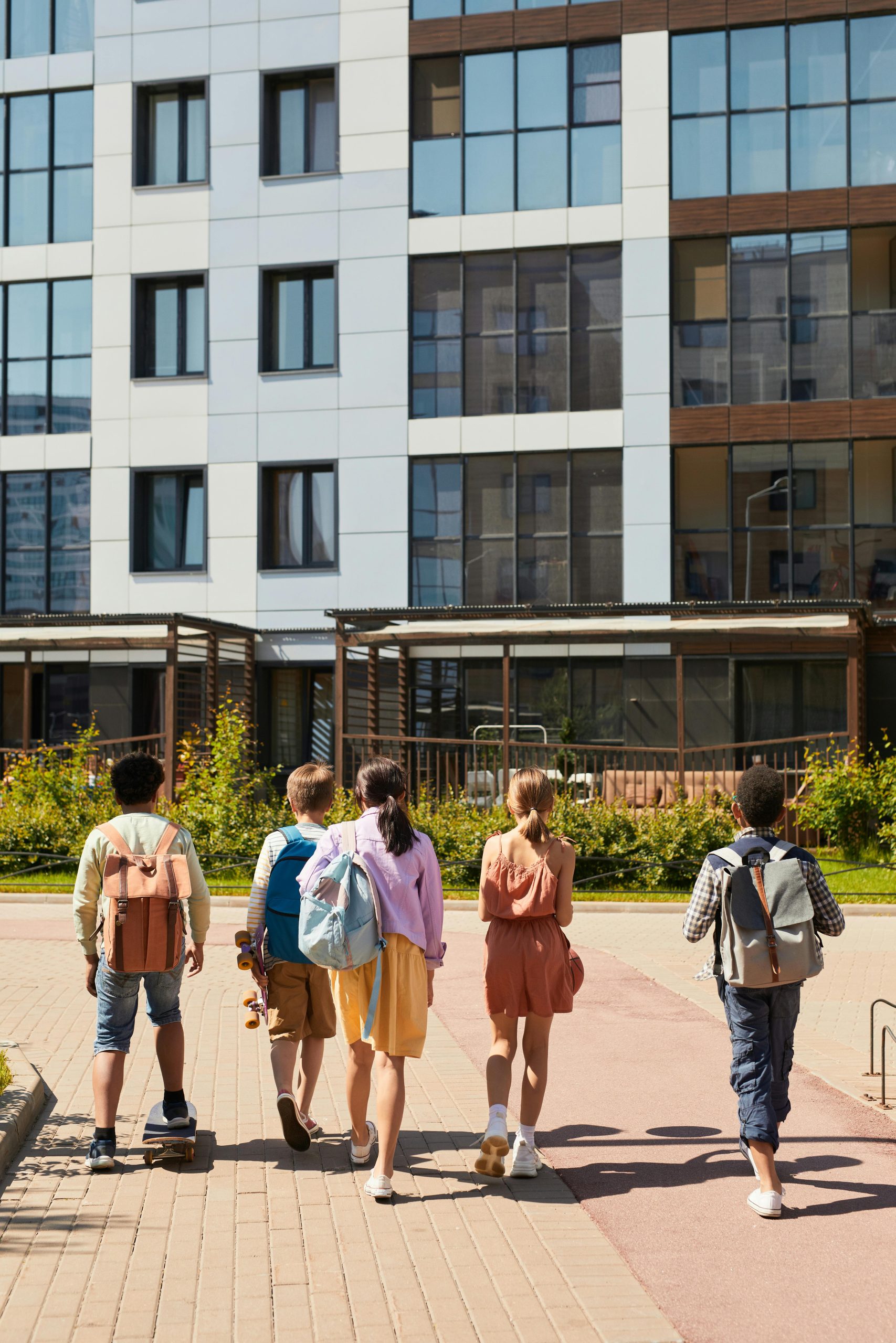 The backs of young students as they walk towards a building
