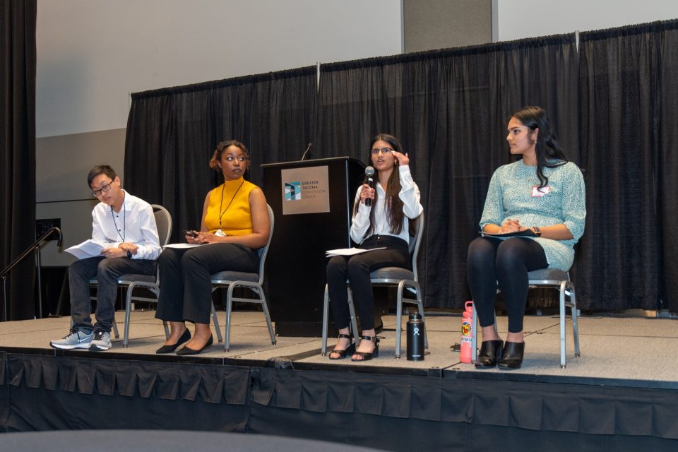 Four students sitting on stage with one speaking