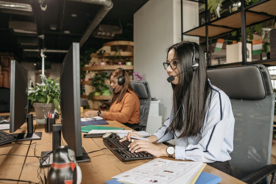 Two women wearing headsets using computers